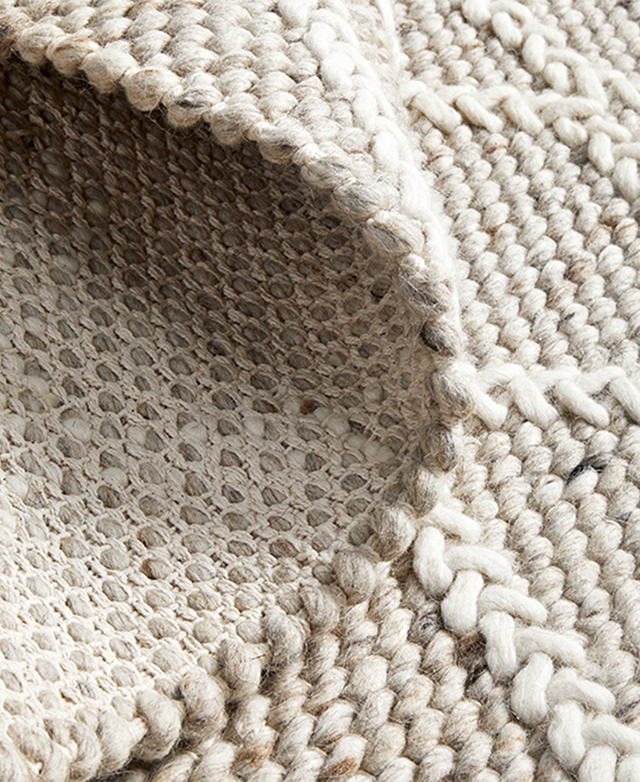 A close-up of the rug folded back demonstrates the speckled nature of the wool-blend weave.