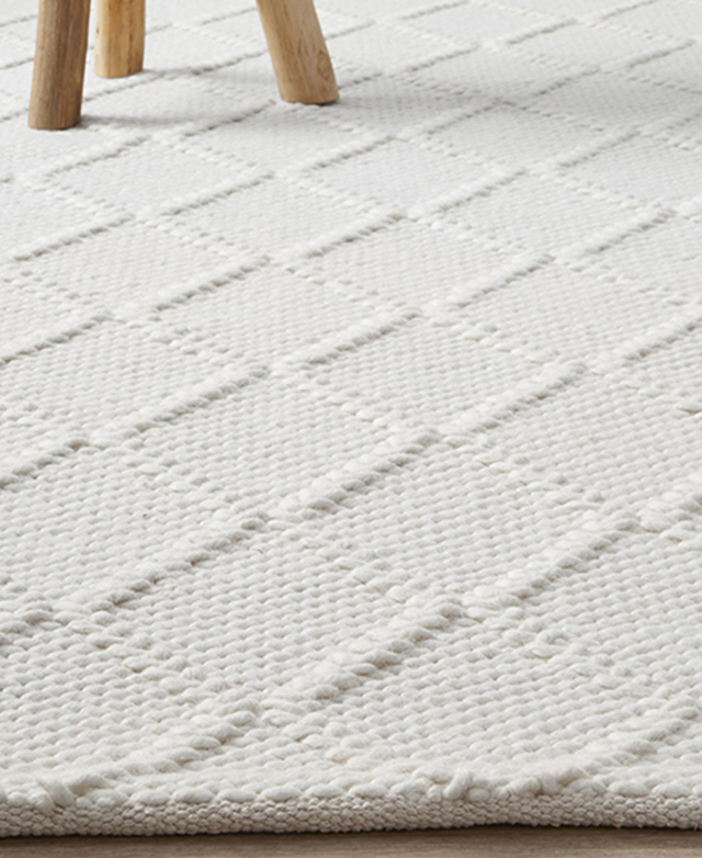 A side view of the rug, close to the ground, highlights a tightly bound edge and the lightly textured lattice pattern.