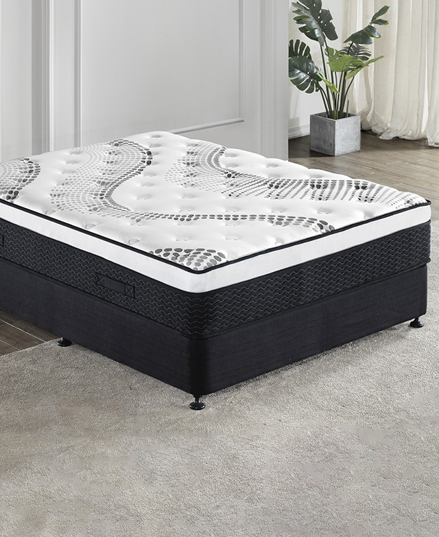 The mattress is positioned on a simple black upholstered base, partially on a cream rug in a light room.