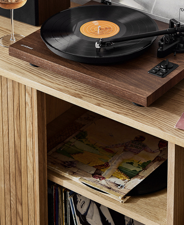 A record player with the lid open, a record on, and a glass of wine, adorn the top. Records are inside the open cupboard.