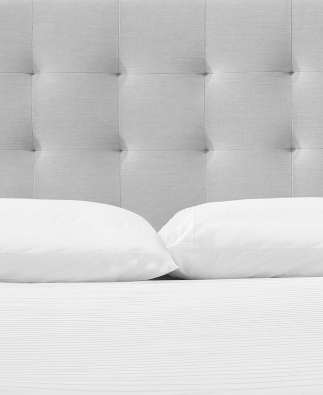 The grid-like quilted tufting of the light grey bedhead is in focus. The grid-like quilted tufting of the light grey bedhead is in focus.