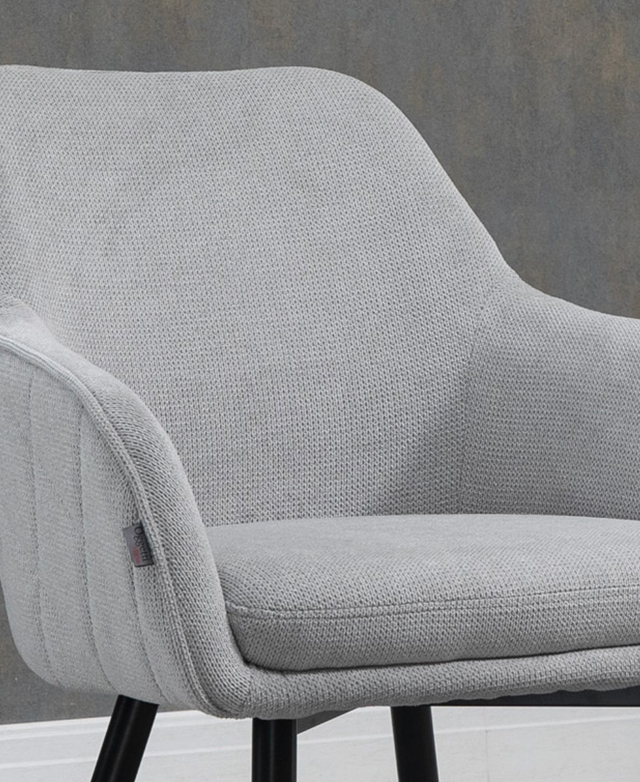 A three-quarter angle of the light grey dining chair displays the curved edges, soft seat and piping trim details.