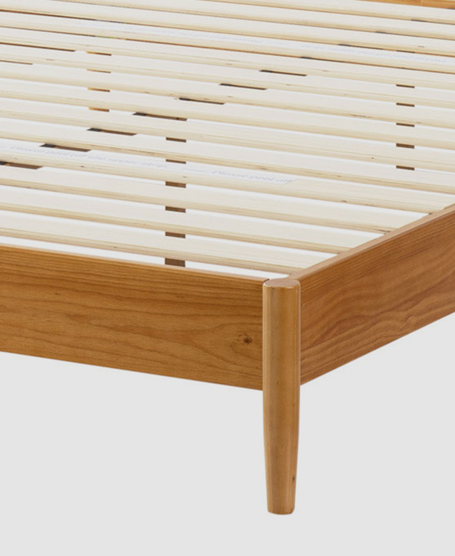 A three-quarter angle from the front zones in on one cylindrical leg, a section of the simple base structure, and the slats. A three-quarter angle from the front zones in on one cylindrical leg, a section of the simple base structure, and the slats.