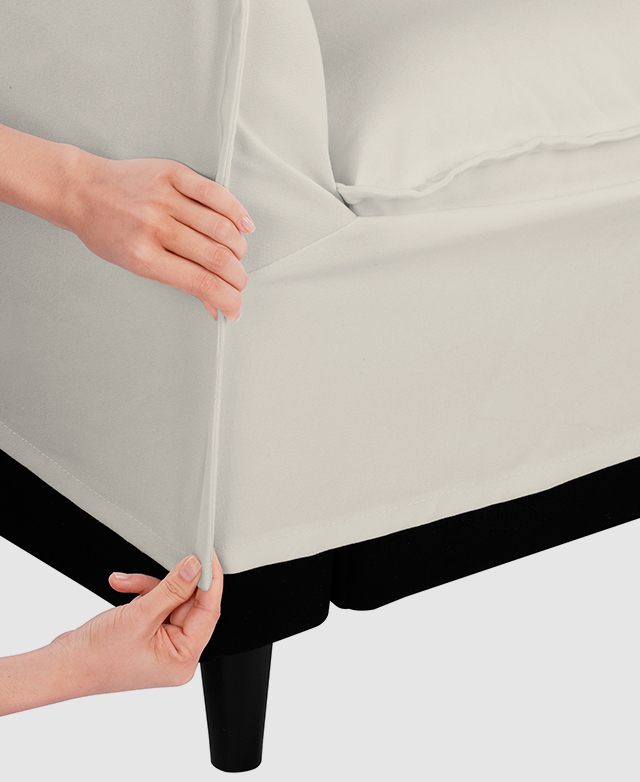 The slipcover is lifted up slightly from the chair's base by two hands that hold the fabric.