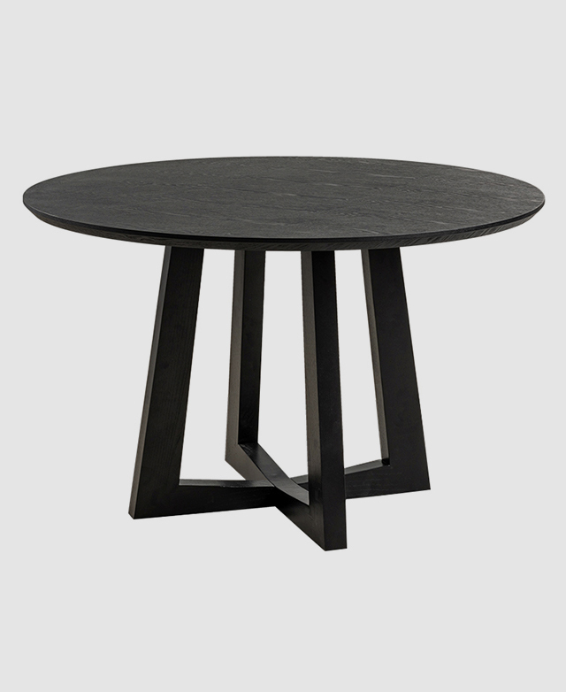 A modern round dining table made of timber with a sculptural cross base.