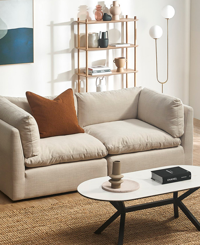 A two-seater modular sofa with cream upholstery and plump cushions is styled in a contemporary living room setting.