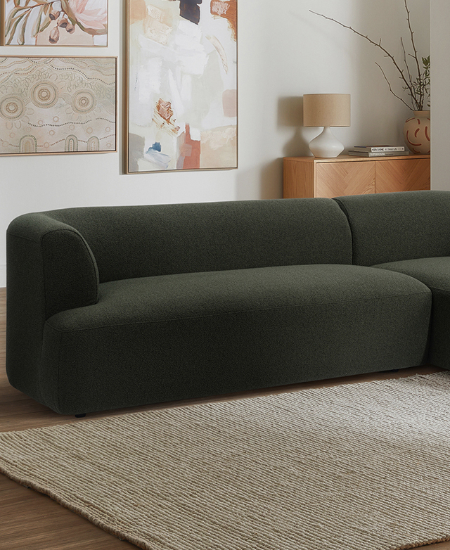 The clean-lined green sofa is positioned next to a cream rug in front of an art-filled wall. The clean-lined green sofa is positioned next to a cream rug in front of an art-filled wall.