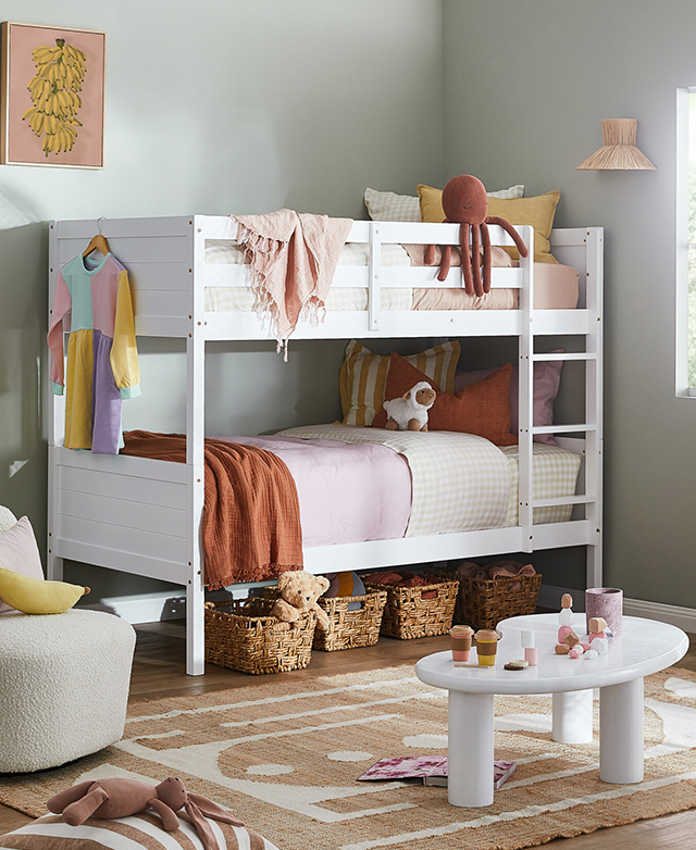 A bright and colourful bedroom scene, with a white bunk bed dressed in layers of bedding, cushions and toys. A bright and colourful bedroom scene, with a white bunk bed dressed in layers of bedding, cushions and toys.