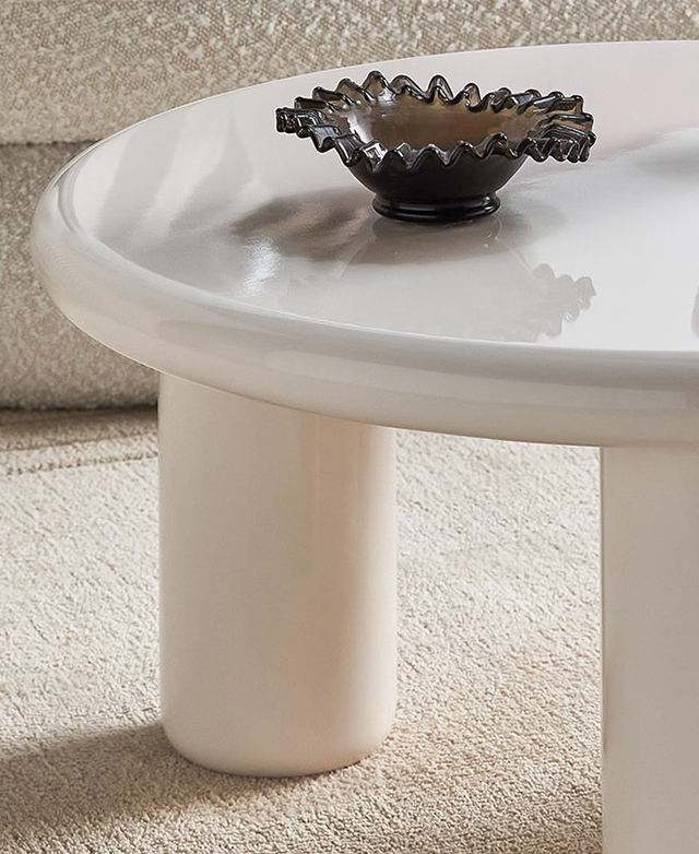 Cropped view highlights the rounded edge of a white coffee table, which has a brown scalloped glass bowl on top Cropped view highlights the rounded edge of a white coffee table, which has a brown scalloped glass bowl on top