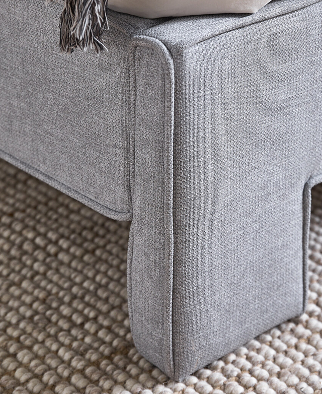 Cropped view of the grey upholstered bed highlights the footend and side panel and their reinforcing piped trims.