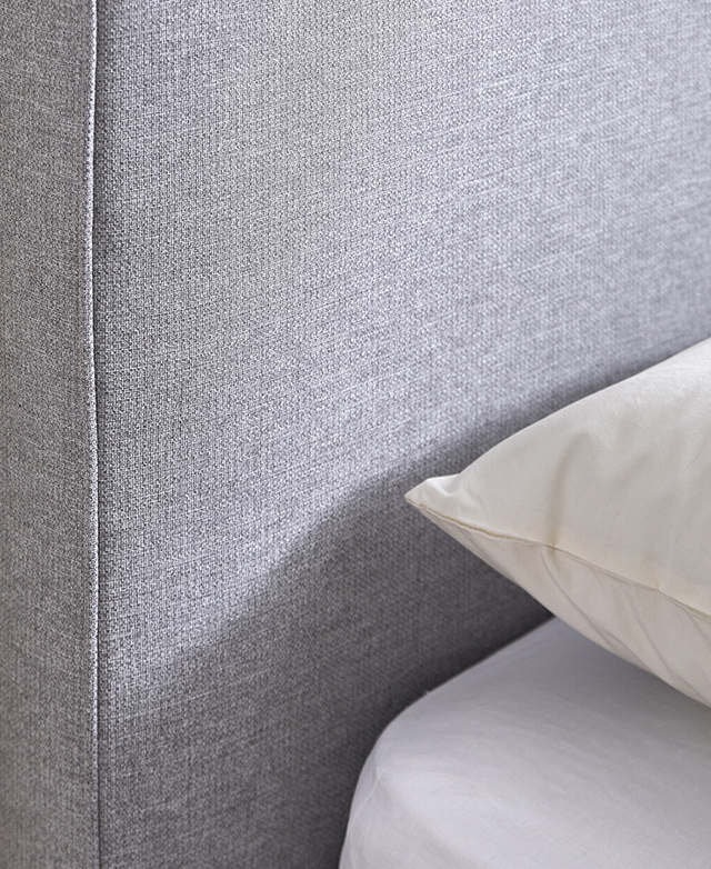 The grey softly-textured weave of the bed's upholstery is shown next to crisp bedding.
