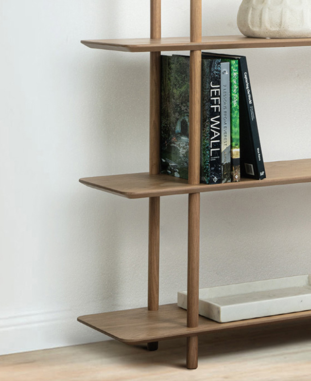 One end of the bookcase is shown against a white wall, with books and decorative items on its shelves. One end of the bookcase is shown against a white wall, with books and decorative items on its shelves.