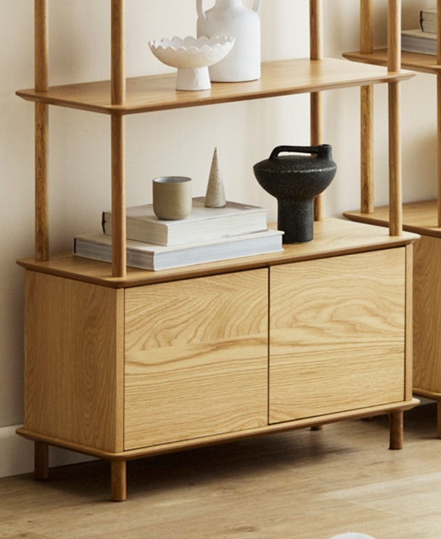 The bookcase is styled in a warmly-lit room on a timber floor, with decorative items on its two lower shelves. The bookcase is styled in a warmly-lit room on a timber floor, with decorative items on its two lower shelves.