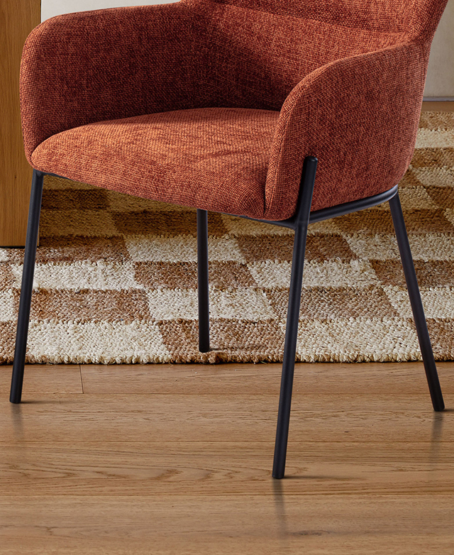 Three-quarter angle of the lower section of the rust armchair draws attention to the sleek, black metal legs.