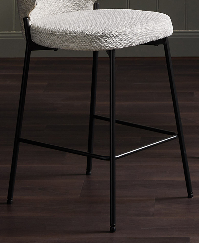 Three-quarter angle of a bar stool zooms in on the black iron tubular legs and frame, shown on a dark timber floor.