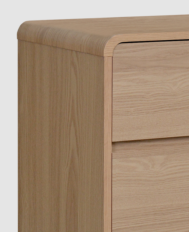 Close view of a waterfall-style top edge of the chest of drawers presents its smooth finish.