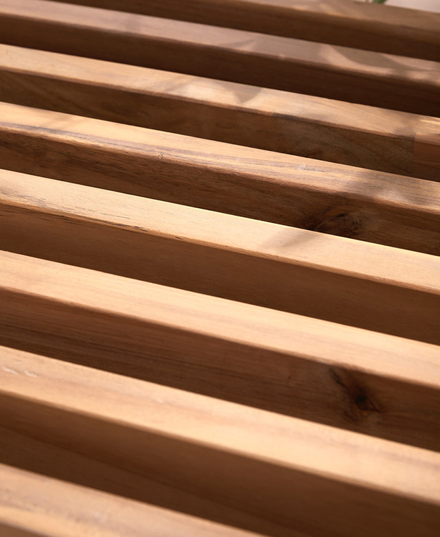 Dappled light lands on the slatted surface of the acacia wood bench. Dappled light lands on the slatted surface of the acacia wood bench.