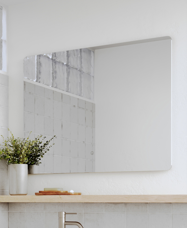 The rectangular mirror is on a white wall over a timber shelf, reflecting glass tiles in a bathroom.