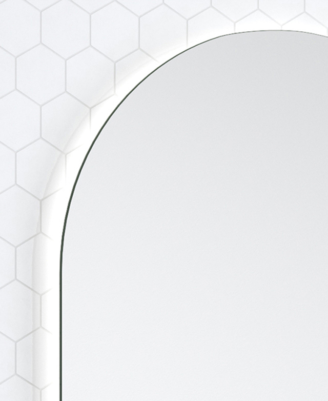 The curved top edge of the frameless mirror is illuminated by an unseen LED strip.