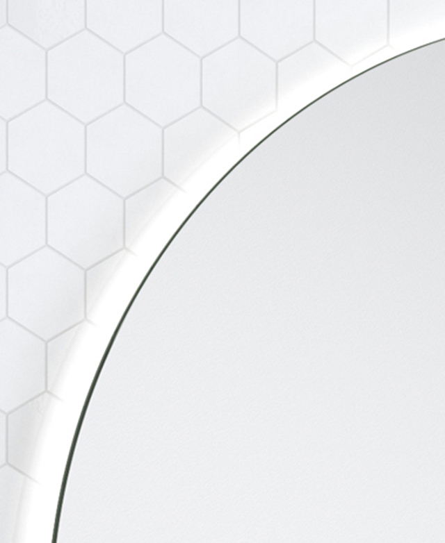 The top edge of the round frameless mirror is illuminated by an unseen LED strip.