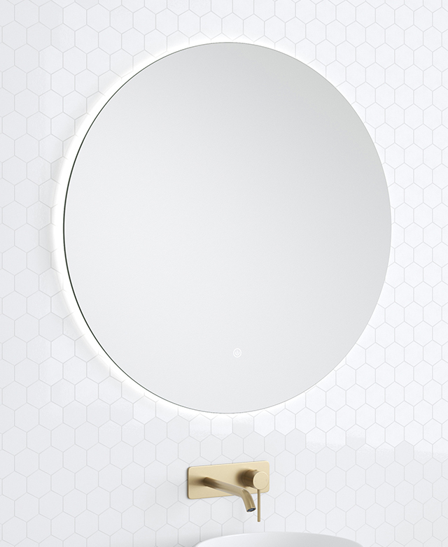 The frameless round bathroom mirror is pictured against a white tiled wall above a brass mixer.