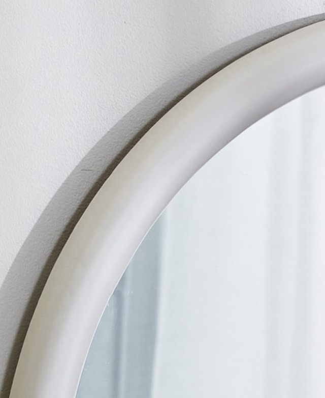 Close up of the top edge of the white round mirror to show its smooth finish against a white wall.