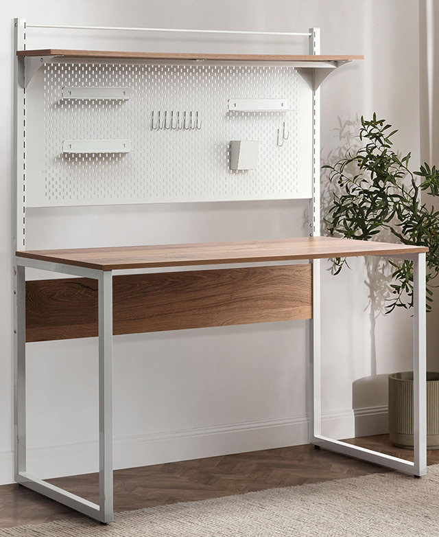 The full desk and pegboard are in the frame, against a white wall with a plant next to it. The full desk and pegboard are in the frame, against a white wall with a plant next to it.