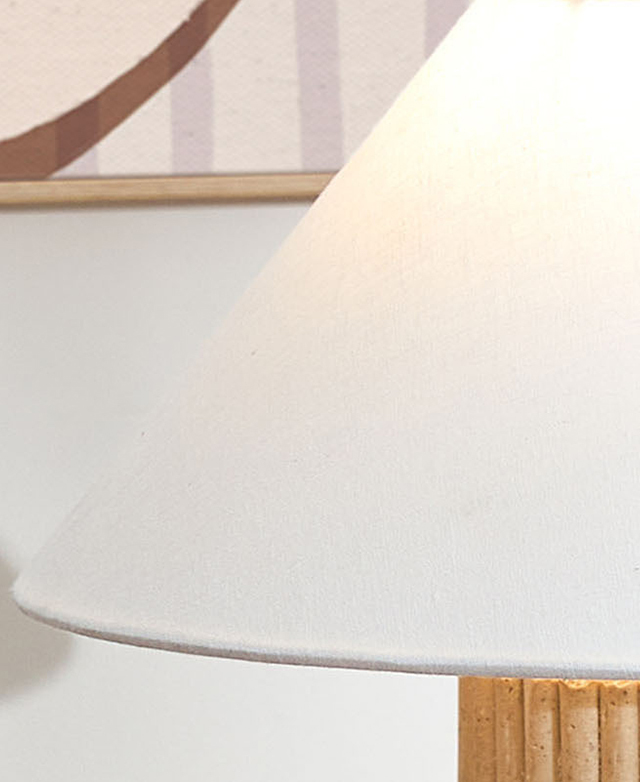 Cropped view of the white fabric empire lamp shade dispersing the glare from an illuminated bulb. Cropped view of the white fabric empire lamp shade dispersing the glare from an illuminated bulb.