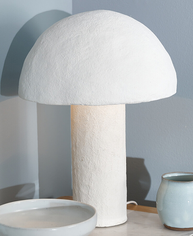 The white mushroom lamp is styled in front of a blue wall, next to smooth ceramics to highlight its organic, textured form.