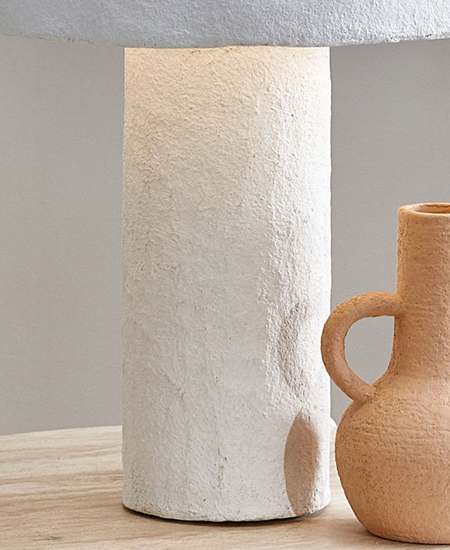 The white cylindrical lamp base has a roughened, matte texture; it's next to a terracotta vase.