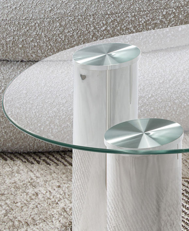 Polished pillar legs and the clear glass top of the coffee table contrast with the soft boucle furniture in the background.