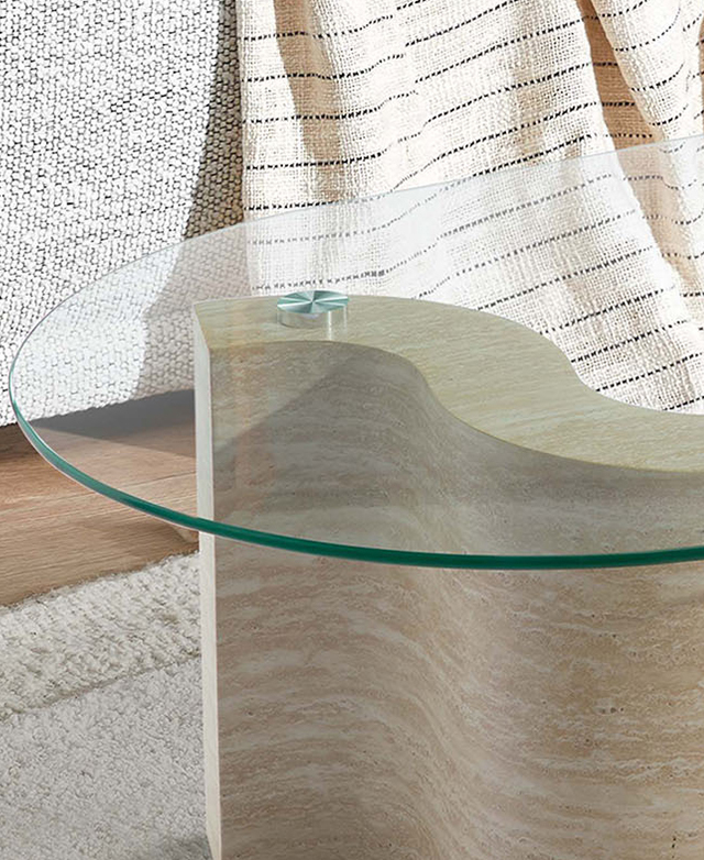 The rounded glass coffee table top is transparent, showing the stone-look base through it; it's styled on a cream rug. The rounded glass coffee table top is transparent, showing the stone-look base through it; it's styled on a cream rug.