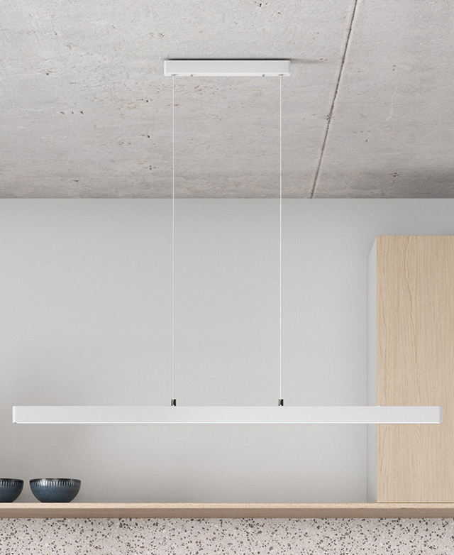 The linear, white pendant light is hung from a concrete ceiling in a contemporary, bright kitchen. The linear, white pendant light is hung from a concrete ceiling in a contemporary, bright kitchen.