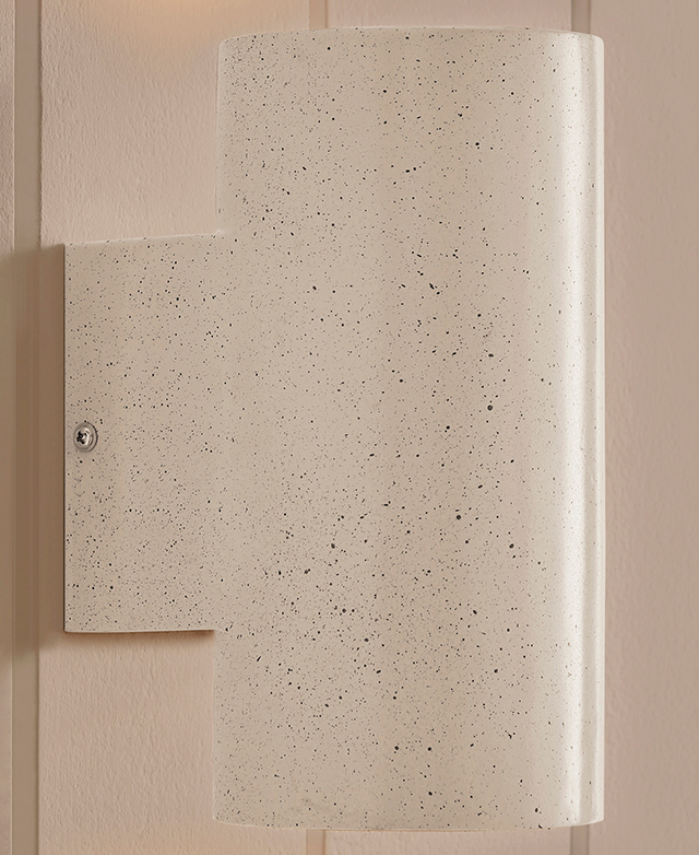 The speckled, cylindrical wall sconce is fixed to a similarly-coloured panelled wall.