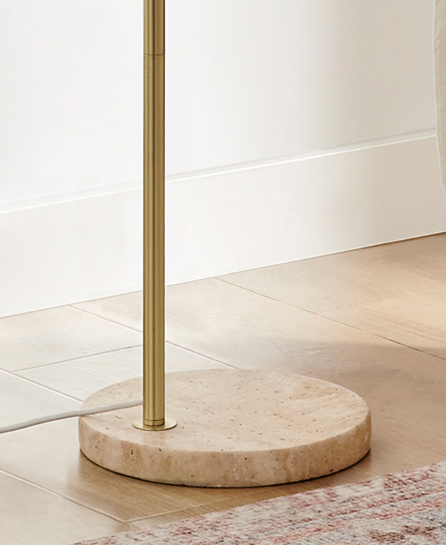 The simple round travertine lamp stand displays natural veins and peachy tones on a timber floor.