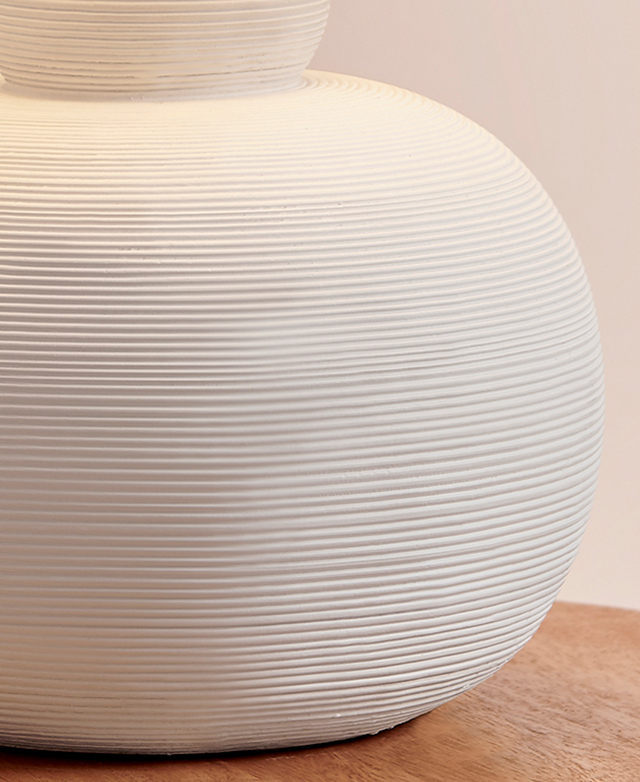 Subtle grooves form concentric circles around the rounded, white polyresin lamp base.