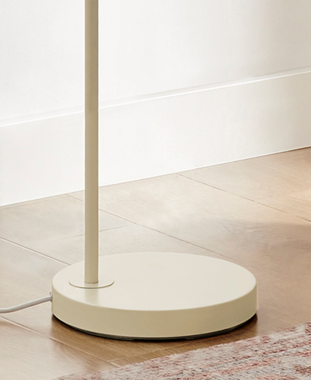 The round cream lamp stand is pictured on a timber floor next to a soft-hued rug.