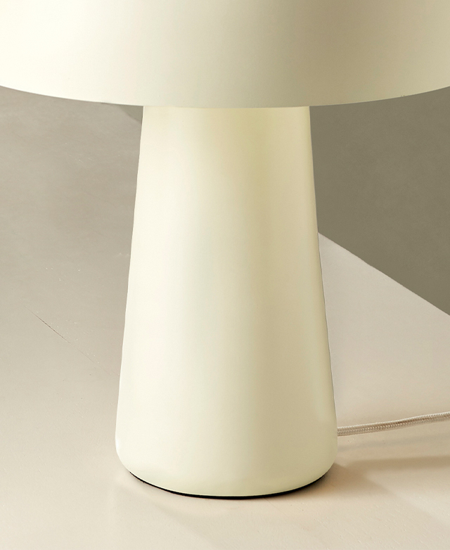 The gently tapered white lamp base, which is positioned on a white surface, is zoomed in on.