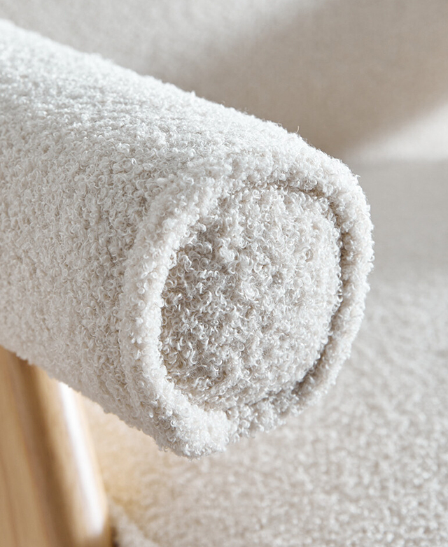 Close up of the end of a cylindrical armrest shows the piping trim and the curly cream upholstery. Close up of the end of a cylindrical armrest shows the piping trim and the curly cream upholstery.