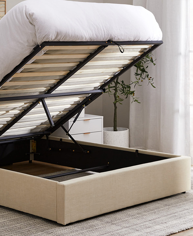 The mattress-topped slatted base is lifted to reveal storage space within the neutral bed frame. The mattress-topped slatted base is lifted to reveal storage space within the neutral bed frame.
