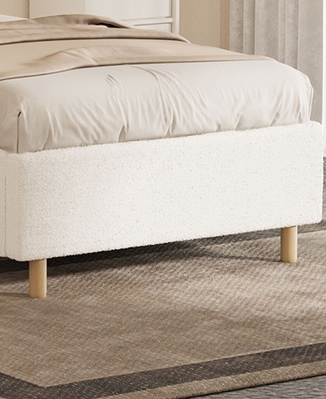 The footend of the bed is on a taupe rug. Two, cylindrical rubberwood legs support the boucle-upholstered bed frame. The footend of the bed is on a taupe rug. Two, cylindrical rubberwood legs support the boucle-upholstered bed frame.