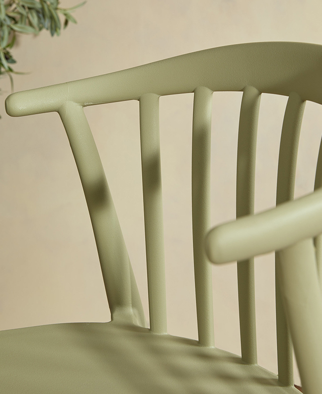 The green seat is displayed close up at an angle to show off the spindle backrest; shadows and light play across the chair.