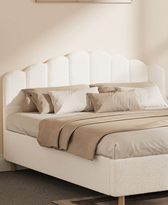 A three-quarter angle depicts the bed dressed in taupe and stone bedding in a bright bedroom. A three-quarter angle depicts the bed dressed in taupe and stone bedding in a bright bedroom.