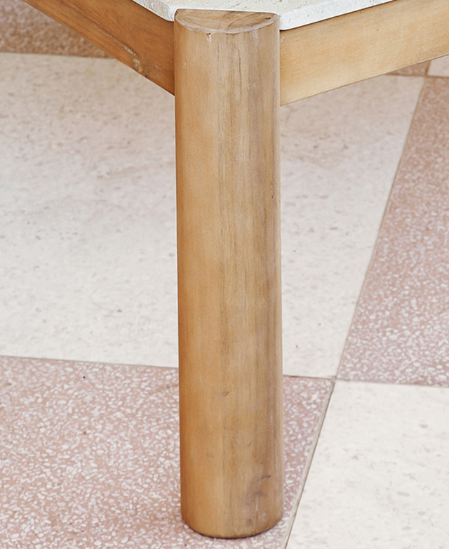 A cylindrical acacia wood coffee table leg is positioned on a clay and white tiled floor.