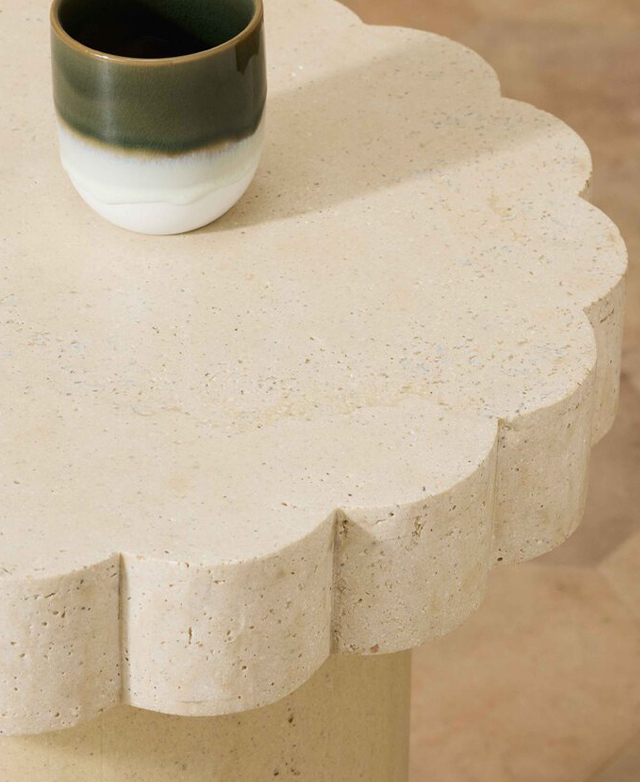 An angled view of the side table highlights the scalloped edge and the flat top surface that holds a green and white mug. An angled view of the side table highlights the scalloped edge and the flat top surface that holds a green and white mug.