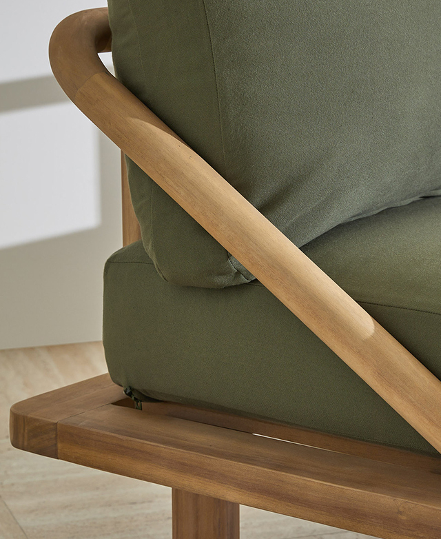 The sloping acacia wood armrest is cylindrical, and frames an end of the daybed with green cushions.