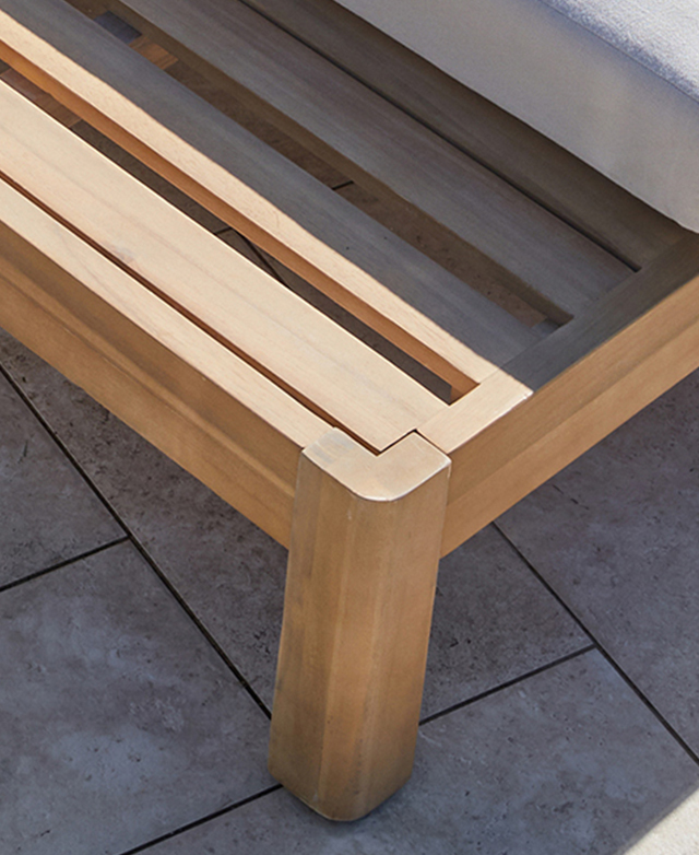 Sunlight shines on the end of the acacia wood sun lounger frame.