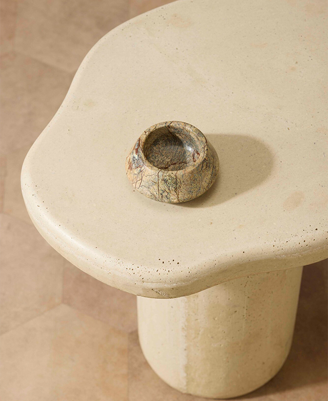 A top-down view of the curvy-edged stone side table with a green and brown marble bowl on the top. A top-down view of the curvy-edged stone side table with a green and brown marble bowl on the top.