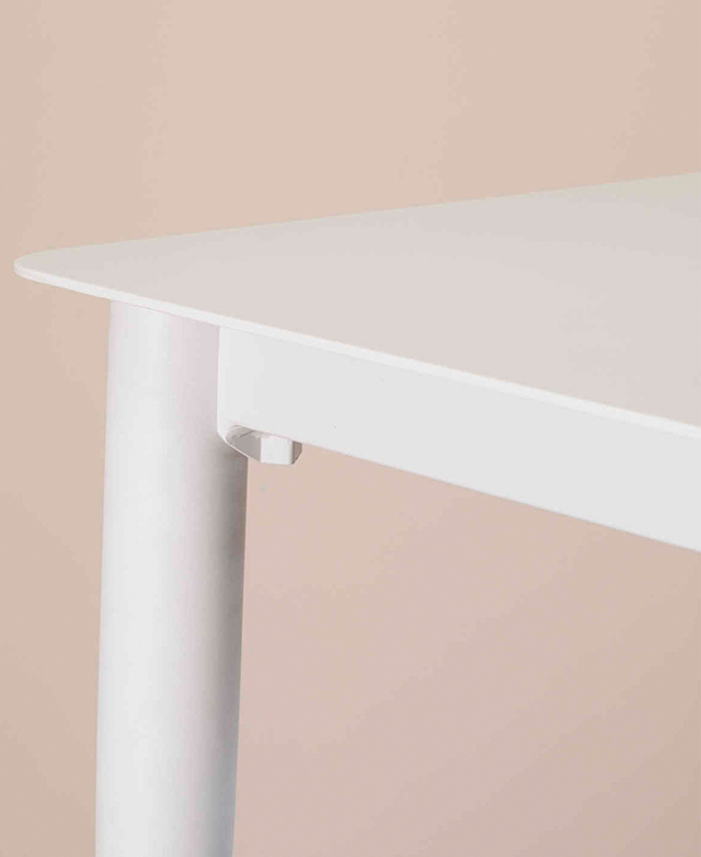 One of the rounded corners of the white dining table is shown from a three-quarter side view. One of the rounded corners of the white dining table is shown from a three-quarter side view.