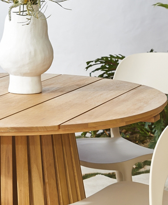 The broad slats of the round dining table are made with eucalyptus wood. A ceramic vase of flowers is on top.